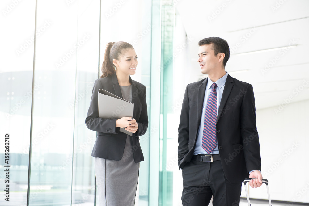 Businessman walking and pulling luggage handle while talking with a businesswoman Businessman walking and pulling luggage handle while talking with a businesswoman
