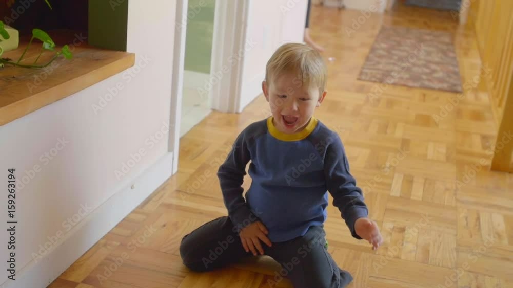 Adorable little boy rolls soccer ball around on wood hallway floor in his home, being silly Adorable little boy rolls soccer ball around on wood hallway floor in his home, being silly