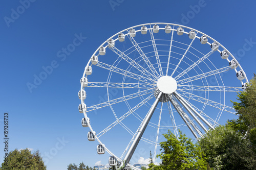 white metal Ferris wheel with cabins on background of blue sky, attraction