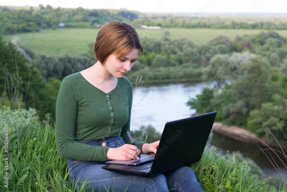 Beautiful young girl using her graphic tablet sitting in the grass Beautiful young girl using her graphic tablet sitting in the grass