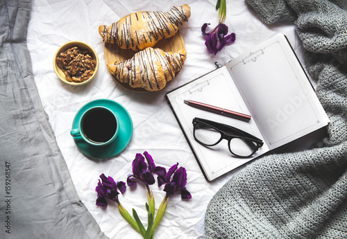 Breakfast in the bed. Morning, croissant, coffee, flowers and a notebook with a pen. Planning