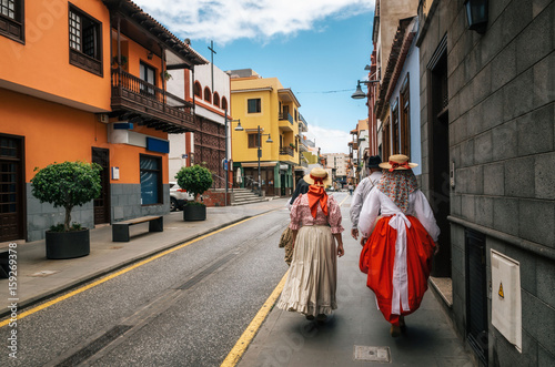 A group of locals in Canarian traditional clothes walk along the street of Puerto de la Cruz with colorful houses. Celebration of the Day of Canary Islands. View from the back. Tenerife, 30 may, Spain photo