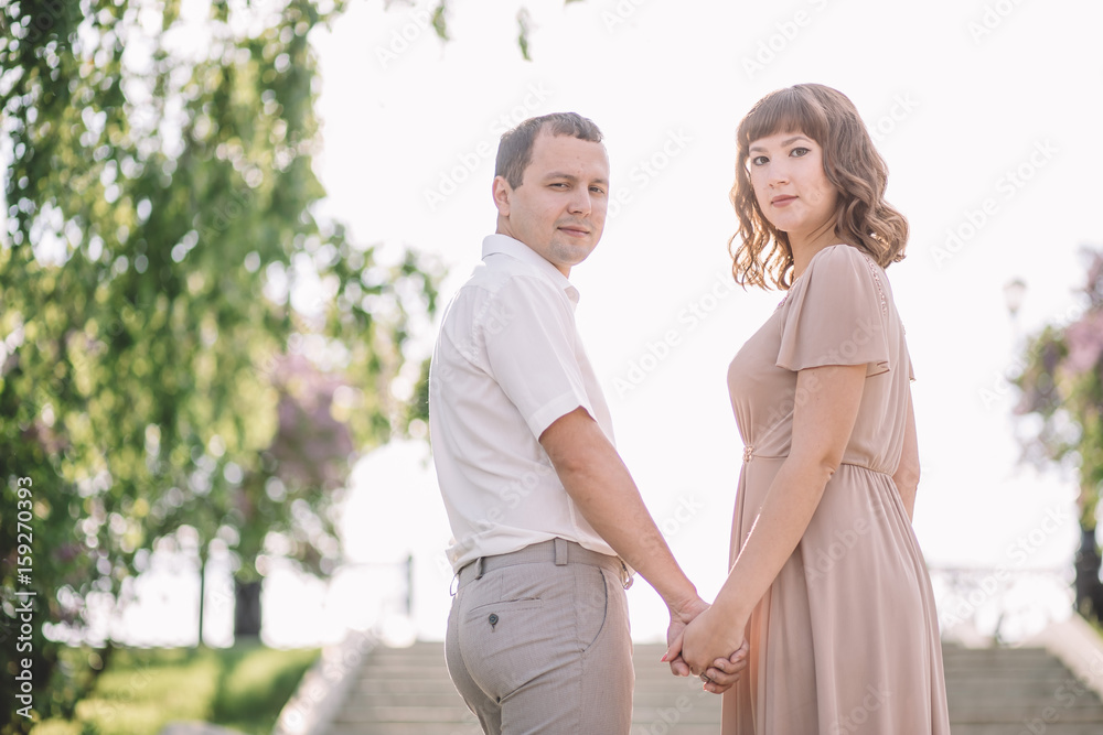 beautiful couple on a walk, the girl in the beige dress and the guy in bright clothes standing on the stairs, holding hands, Park, summer, nature