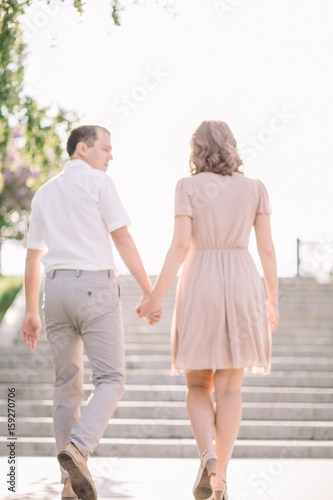 beautiful couple on a walk, the girl in the beige dress and the guy wearing light clothing go up the stairs back, holding hands, Park, summer, nature photo