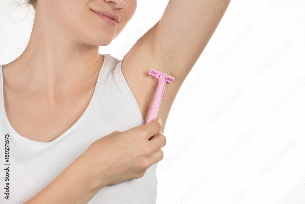 Beautiful young woman in a T-shirt is smiling and doing a depilation of armpits or shaving underarms pink razor on a white background Beautiful young woman in a T-shirt is smiling and doing a depilation of armpits or shaving underarms pink razor on a white background