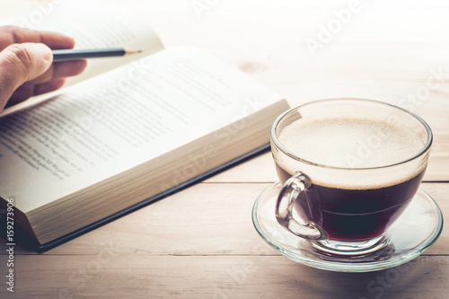 Male hand with Pencil on book and coffee cup on wood table in morning