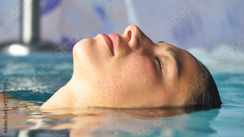 Beautiful young girl (woman) relaxed in a hydromassage bath, in a blue bathing suit, on a blue background. Concept: spa procedures, body massages, spa cream, relax, spa water treatments, swimming pool