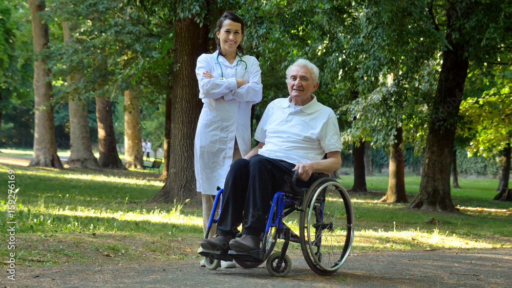 Doctor, nurse, care for the elderly, girl (woman) and grandfather sitting in a wheelchair, walking in the park. Concept: a boarding house, a sanatorium, a house for the elderly, help for the elderly. Doctor, nurse, care for the elderly, girl (woman) and grandfather sitting in a wheelchair, walking in the park. Concept: a boarding house, a sanatorium, a house for the elderly, help for the elderly.