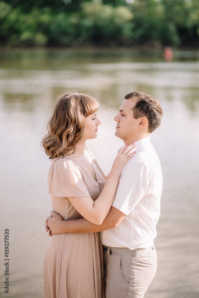 love story, beautiful couple a man and a woman in bright clothes, happy family, walking along the river Bank,standing holding hands, looking at each other, hugging, summer, nature
