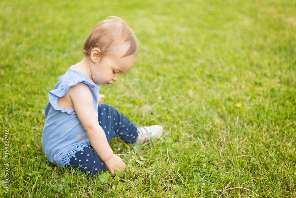 Fourteen months old baby girl sitting in the shadow on the grass on the sunny summer day Fourteen months old baby girl sitting in the shadow on the grass on the sunny summer day