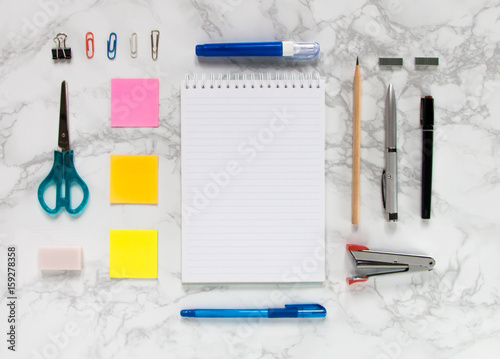 Creative mock-up flat lay of stationery on white marble texture background - Work space concept compose of notebook, post-it, pen, pencil, rubber, clip, scissors, calculator, and stapler
