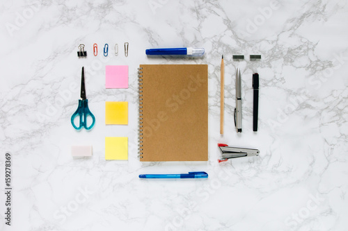 Creative mock-up flat lay of stationery on white marble texture background - Work space concept compose of notebook, post-it, pen, pencil, rubber, clip, scissors, calculator, and stapler