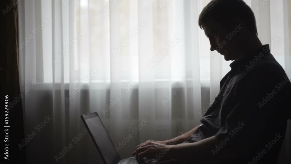 Silhouette of a man with a laptop near a window in the office