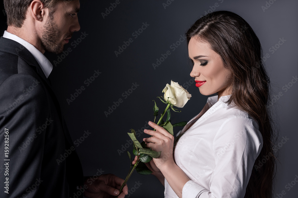 young man in suit presenting white rose to his girlfriend isolated on black young man in suit presenting white rose to his girlfriend isolated on black