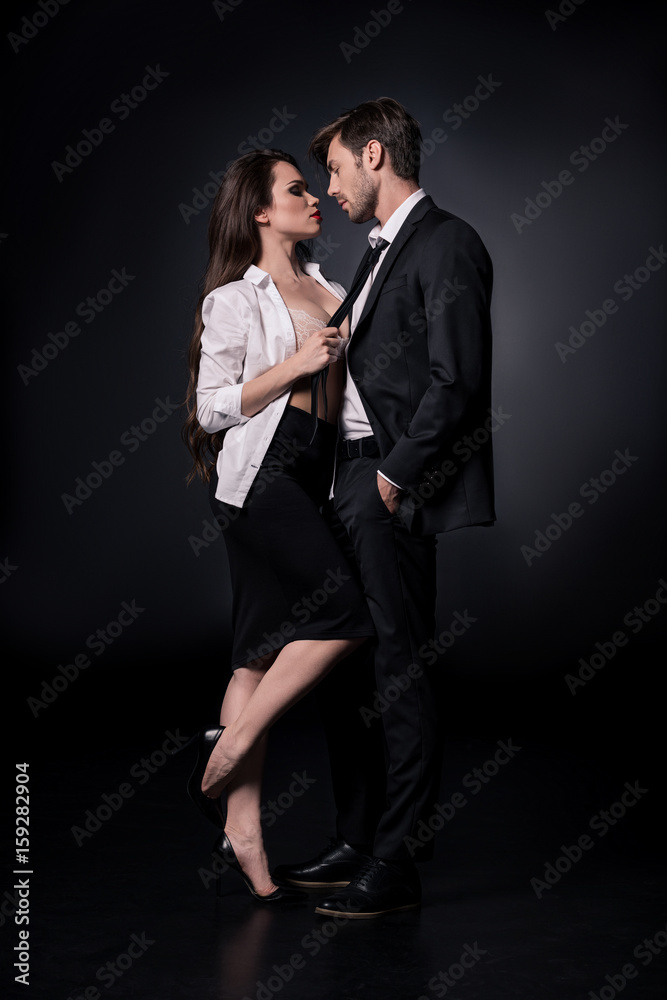 young sexy woman seducing young man in suit isolated on black