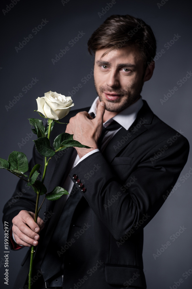 portrait of young man in formal wear holding white rose and looking at camera portrait of young man in formal wear holding white rose and looking at camera