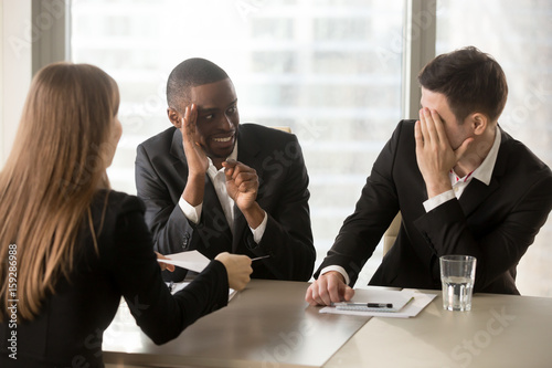 Multiracial businessmen hiding face with hands, sneaking look at each other while businesswoman presenting document, recruiters covertly discussing candidate, secretly whispering during interview photo