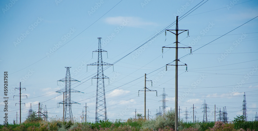 A lot of electric posts and electric wires in the field against the sky.