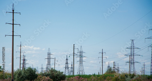 A lot of electric posts and electric wires in the field against the sky.