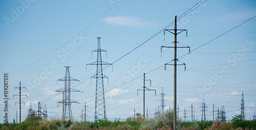 A lot of electric posts and electric wires in the field against the sky.