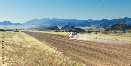 Car driving fast with dust cloud on desert road