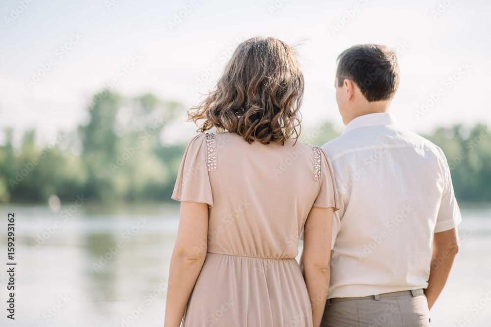 beautiful couple man and woman in a light beige light clothing spend time together, enjoy each other, communicate, are on the river Bank, back, rear view, love story beautiful couple man and woman in a light beige light clothing spend time together, enjoy each other, communicate, are on the river Bank, back, rear view, love story