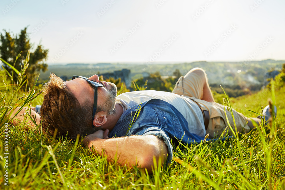 Man lying on grass enjoying peaceful sunny day - obrazy, fototapety, plakaty 
