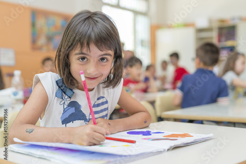 Happy schoolgirl writing on schoolbook in her classroom