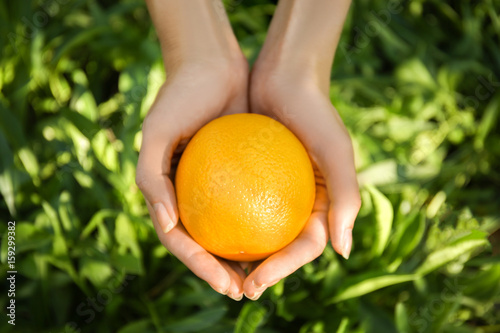 Female hands holding whole orange fruit on green background