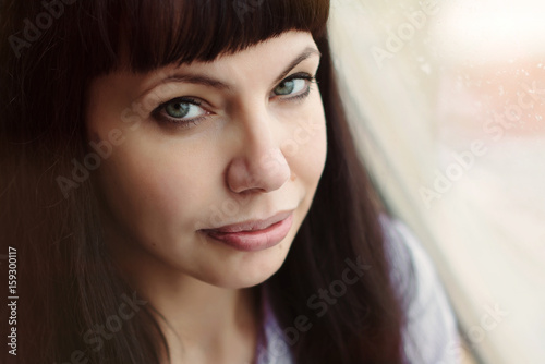 A beautiful middle-aged girl sits on the windowsill near the window. It is raining outside the window.