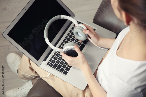 Audio book concept. Young woman using laptop with headphones, close up