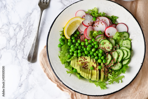 Mix salad with cucumber, avocado, green peas and flax seeds on a marble background