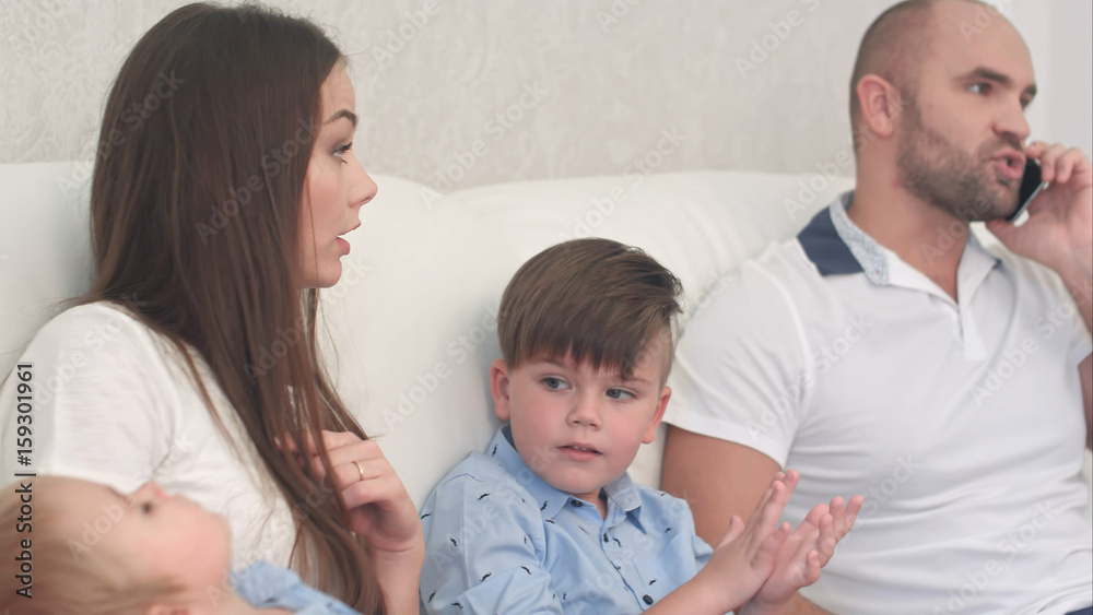 Young mother being angry with her husband talking on the phone and not playing with his sons