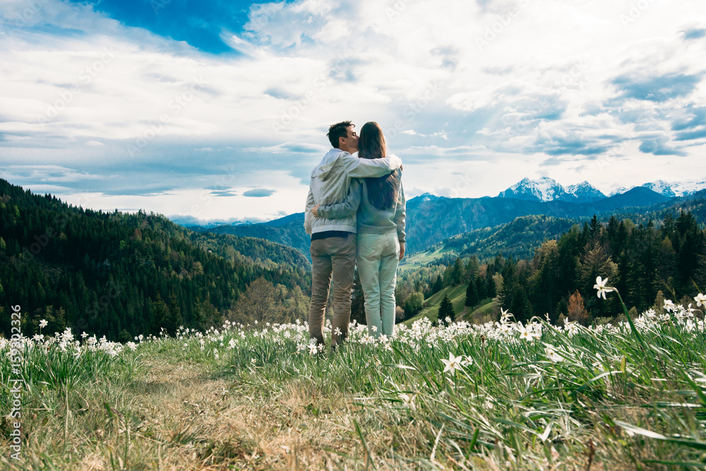 Young couple standing together and looking at mountain landscape and cloudy sky.