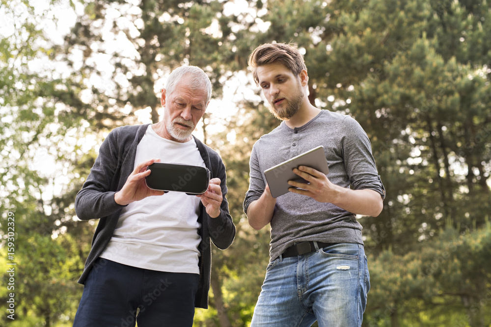 Obraz premium Young man and his senior father with VR glasses outdoors.