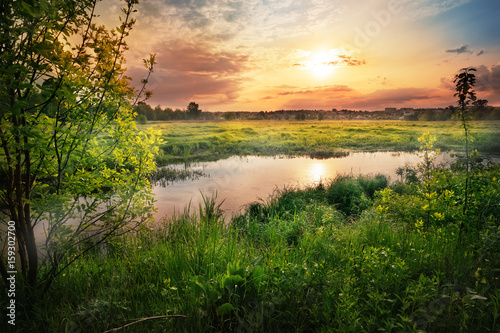 Sunset on the river with green grass and trees on the shore