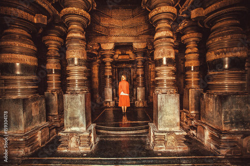 Lonely woman standing in center of ancient Hindu temple with stone columns, India. Traditional architecture of Asia.