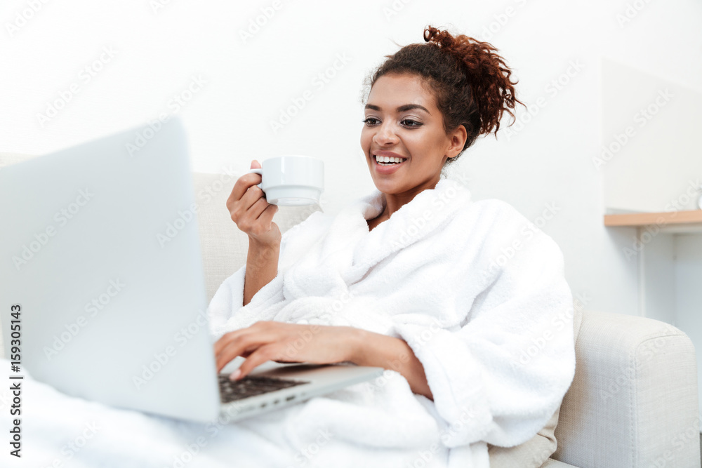Young african lady sitting on sofa drinking coffee Young african lady sitting on sofa drinking coffee