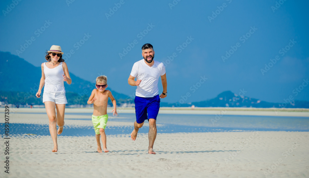 Happy young family of three having fun on the desert sunny beach