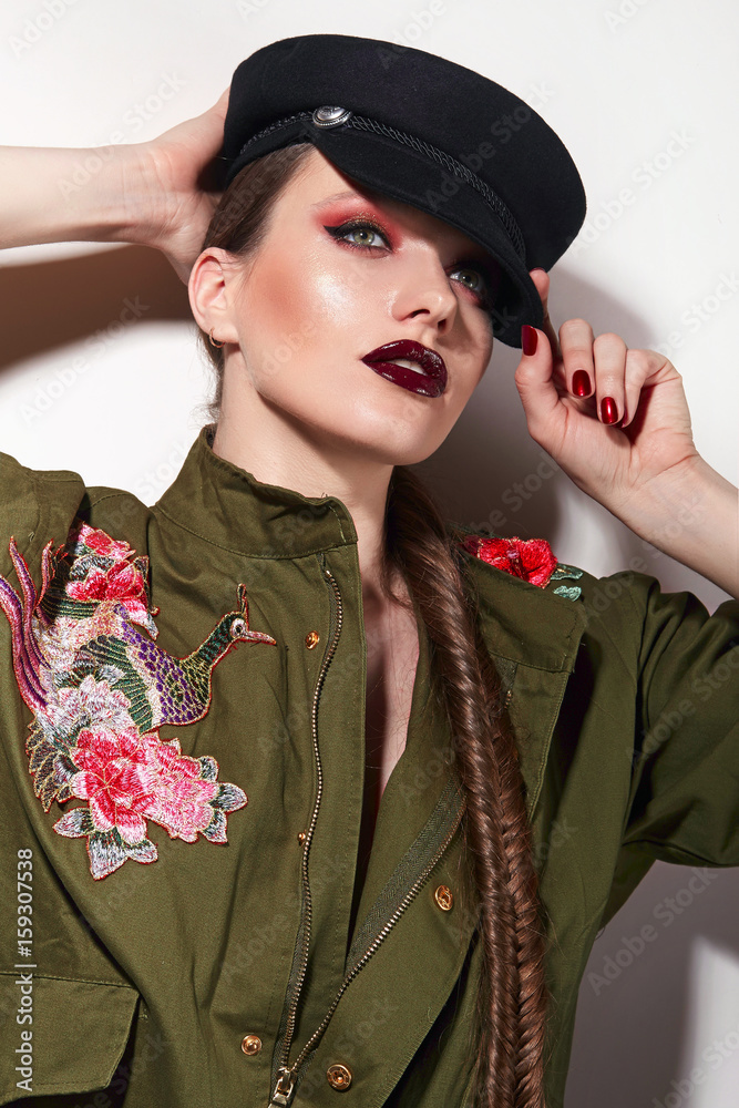 Beautiful young girl with bright make-up in a green trench coat and a black  cap
