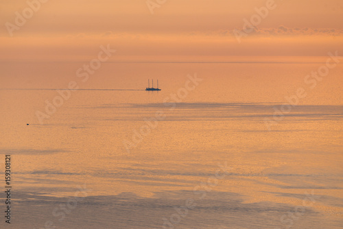 Solo boat sailing in mediterranean sea in summer at sunrise sunset