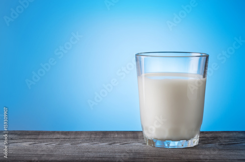 Glass of milk on wooden table with blue background