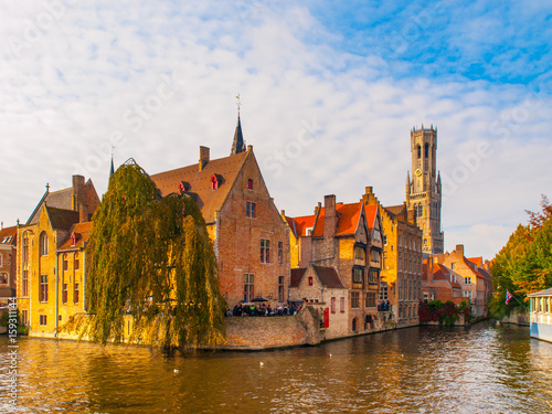Cityscape of Bruges, Flanders, Belgium. Water canal at Rozenhoedkaai with old brick buildings and Belfry Tower on background.
