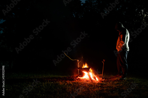 traveler standing near campfire in the forest in night, copy space