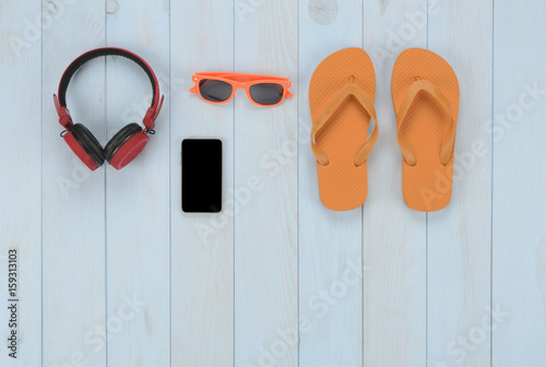 Artículos de ocio sobre fondo de madera azul: chanclas, auriculares, smart phone y gafas de sol
