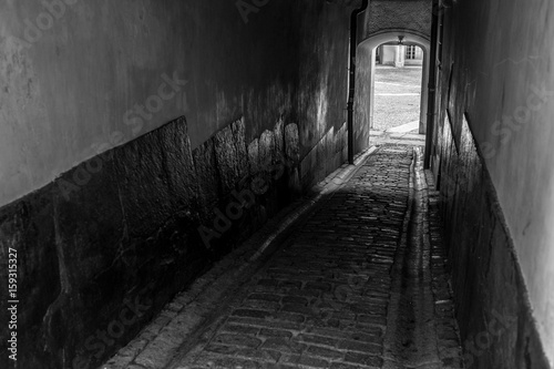 A narrow dark and a little mysterious passage, covered with cobblestones between two small alleys in the old town of Stockholm, with a bright opening at the far end