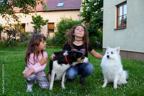 Zwei Geschwister mit Hunden erholen sich im Garten am Haus photo