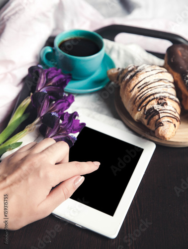 Delicious breakfast in bed with flowers. Croissant with coffee and a tablet for rest photo