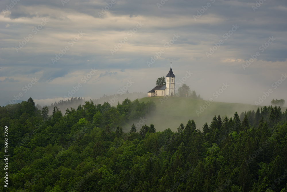 Jamnik church on a hillside in the spring, foggy weather at sunset in Slovenia, Europe. Mountain landscape shortly after spring rain. Slovenian Alps. Jamnik church on a hillside in the spring, foggy weather at sunset in Slovenia, Europe. Mountain landscape shortly after spring rain. Slovenian Alps.