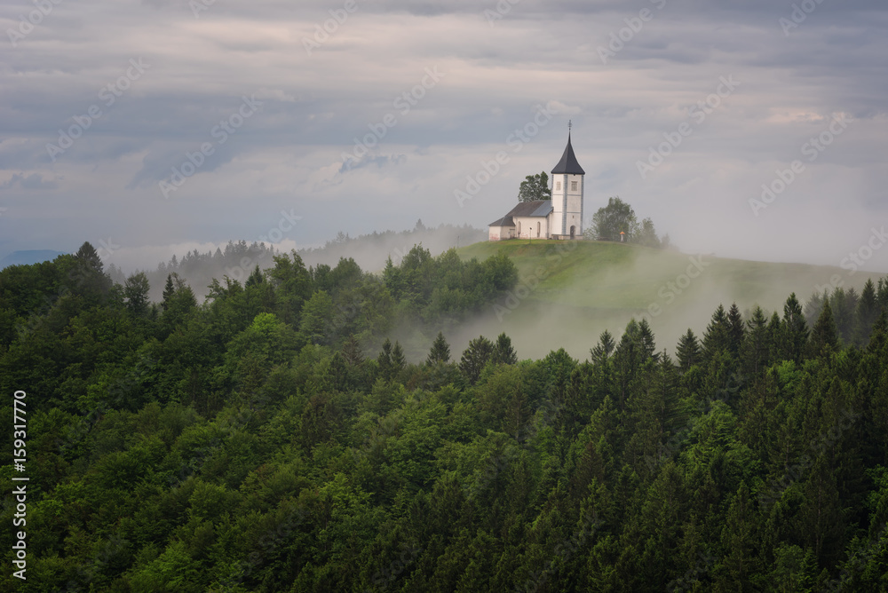 Jamnik church on a hillside in the spring, foggy weather at sunset in Slovenia, Europe. Mountain landscape shortly after spring rain. Slovenian Alps. 
